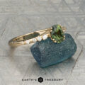 The "Blythe" ring in 14K yellow gold showcases a 0.90-carat Australian sapphire and diamond accents, displayed on a blue-green stone with the "Earth's Treasury" logo below.
