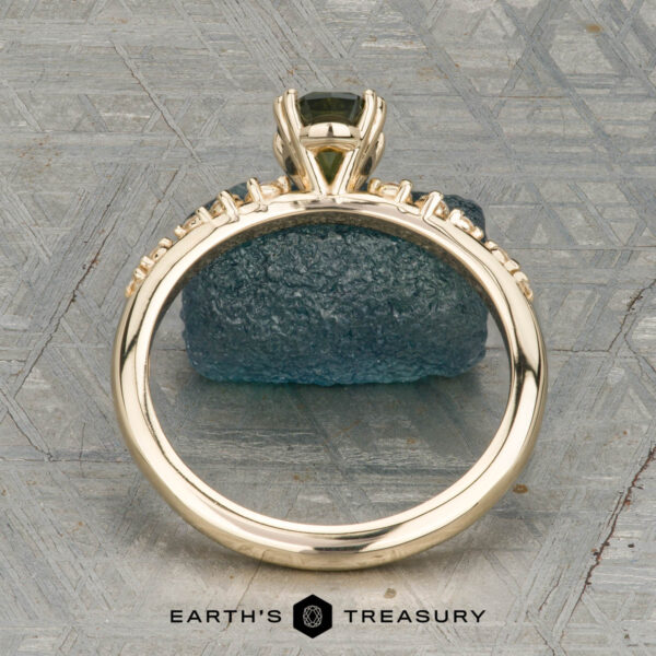 The "Blythe" ring in 14K yellow gold with 0.90-carat Australian sapphire The "Blythe" ring in 14K yellow gold showcases a 0.90-carat Australian sapphire and diamond accents, displayed on a blue-green stone with the "Earth's Treasury" logo below.