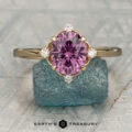gold halo ring with an oval purple gemstone and four small diamonds is shown upright on a rough blue stone, with the "Earth's Treasury" logo displayed below.