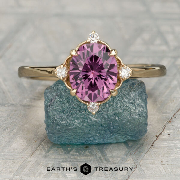 The "Marisol" ring in 14K yellow gold with 1.97-carat Mahenge garnet gold halo ring with an oval purple gemstone and four small diamonds is shown upright on a rough blue stone, with the "Earth's Treasury" logo displayed below.