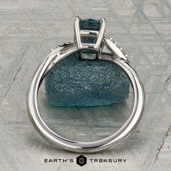 The "Tango" ring in platinum with 1.39-carat Montana sapphire The "Tango" ring in platinum, featuring a 1.39-carat rectangular light blue Montana sapphire and diamond accents, is displayed upright on rough blue mineral with a patterned background and the "Earth's Treasury" logo below.