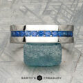A platinum Atlas ring encircling a rough blue gemstone, displayed on a textured gray surface with "Earth's Treasury" at the bottom.