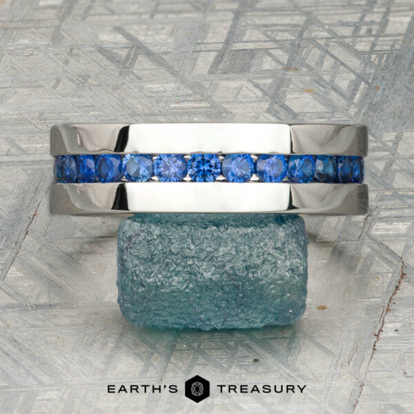 The "Atlas" ring in platinum A platinum Atlas ring encircling a rough blue gemstone, displayed on a textured gray surface with "Earth's Treasury" at the bottom.