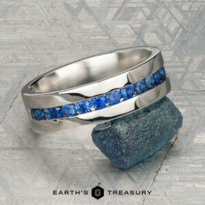 A platinum Atlas ring encircling a rough blue gemstone, displayed on a textured gray surface with "Earth's Treasury" at the bottom.