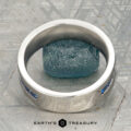 A platinum Atlas ring encircling a rough blue gemstone, displayed on a textured gray surface with "Earth's Treasury" at the bottom.
