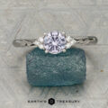 The "Aster" ring in platinum, featuring a 0.80-carat Montana sapphire and accent stones, rests on rough blue crystal with textured geometric patterns in the background.