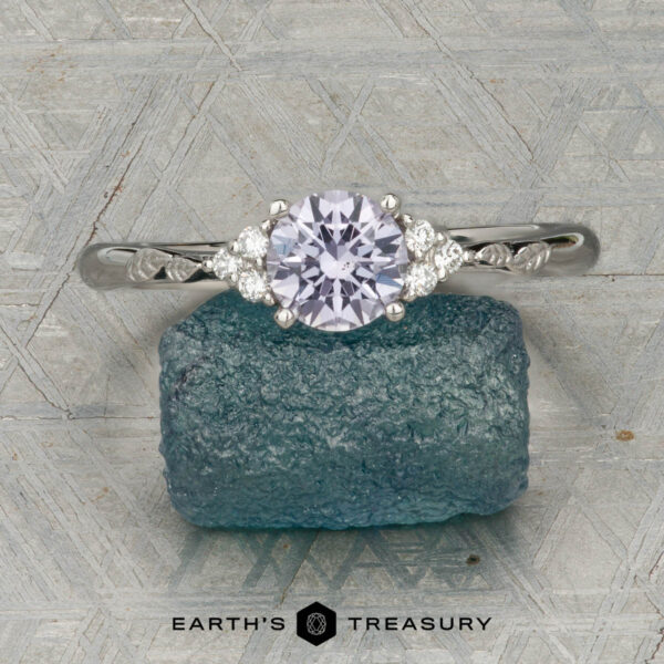 The "Aster" ring in platinum with 0.80-carat Montana sapphire The "Aster" ring in platinum, featuring a 0.80-carat Montana sapphire and accent stones, rests on rough blue crystal with textured geometric patterns in the background.