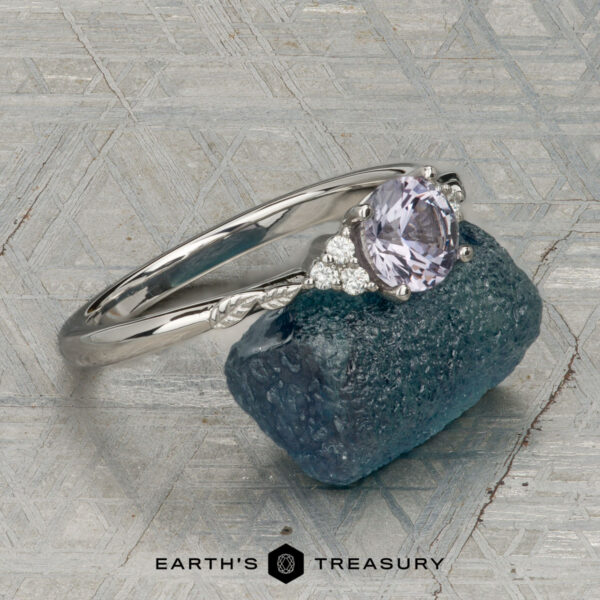 The "Aster" ring in platinum with 0.80-carat Montana sapphire The "Aster" ring in platinum, featuring a 0.80-carat Montana sapphire and accent stones, rests on rough blue crystal with textured geometric patterns in the background.