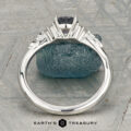 The "Aster" ring in platinum, featuring a 0.80-carat Montana sapphire and accent stones, rests on rough blue crystal with textured geometric patterns in the background.