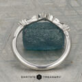 The "Aster" band in platinum, featuring a leaf motif and central diamond, is displayed atop a rough blue gemstone on a patterned surface with the text "EARTH'S TREASURY" below.