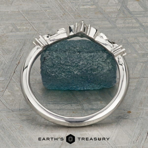 The "Aster" band in platinum The "Aster" band in platinum, featuring a leaf motif and central diamond, is displayed atop a rough blue gemstone on a patterned surface with the text "EARTH'S TREASURY" below.