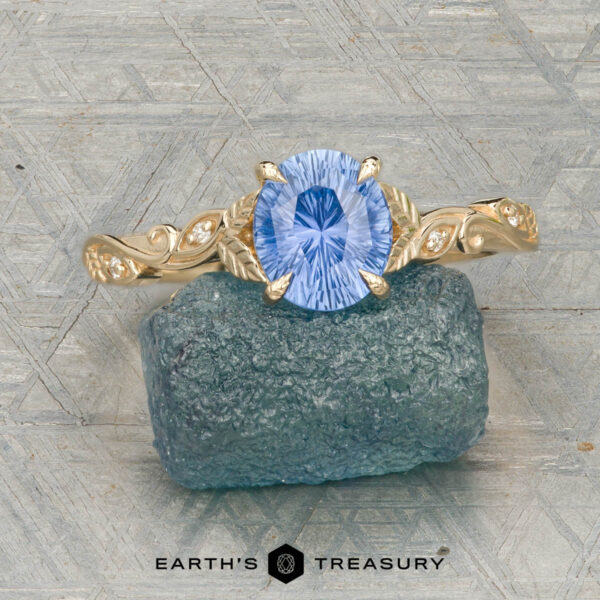 The "Amborella" ring in 14K yellwo gold with 1.23-carat Ceylon sapphire The "Amborella" ring in 14K yellow gold with a 1.23-carat Ceylon sapphire is shown on a rough blue stone, featuring the Earth's Treasury logo at the bottom.