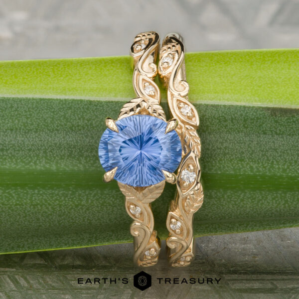 The "Amborella" ring in 14K yellow gold with 1.23-carat Ceylon sapphire, alongside the "Amborella" band in 14K yellow gold The "Amborella" ring in 14K yellow gold with a 1.23-carat Ceylon sapphire, paired with the "Amborella" band in matching gold, shown on a green leaf.