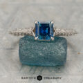 The "Anya" ring, crafted in 14K white gold and set with a 0.87-carat Montana sapphire, is displayed atop a rough blue gemstone.