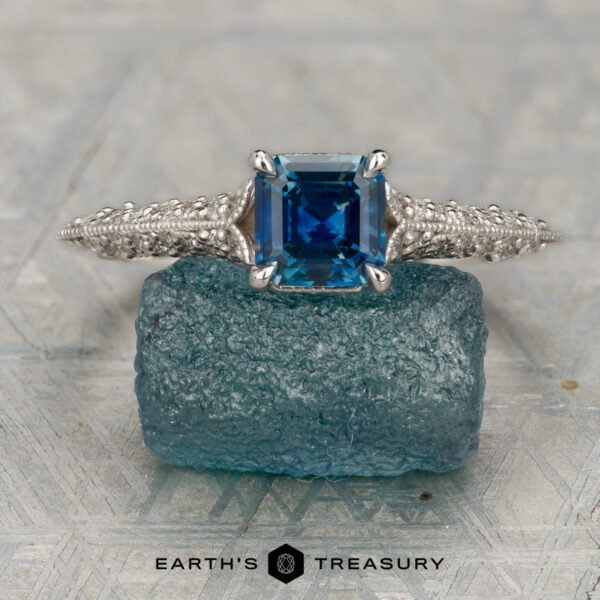 The "Anya" ring in 14K white gold with 0.87-carat Montana sapphire The "Anya" ring, crafted in 14K white gold and set with a 0.87-carat Montana sapphire, is displayed atop a rough blue gemstone.