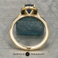 The “Eleanor” ring in 18K yellow gold, featuring a 1.47-carat Montana sapphire and diamond halo, is displayed on rough blue mineral with the Earth’s Treasury logo below.