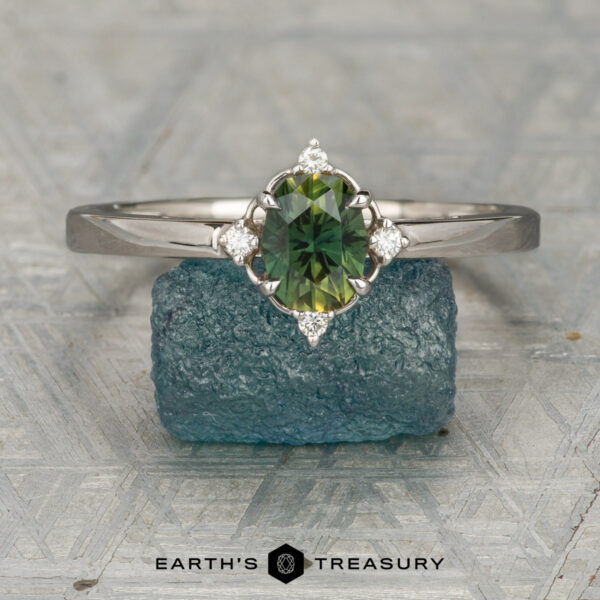 Fischer, Noah and Ashworth, Emoss The Fischer, Noah and Ashworth, Emoss ring features a silver halo with an oval green gemstone and small diamond accents, displayed on a rough blue stone above the Earth's Treasury logo—a unique Marisol design.