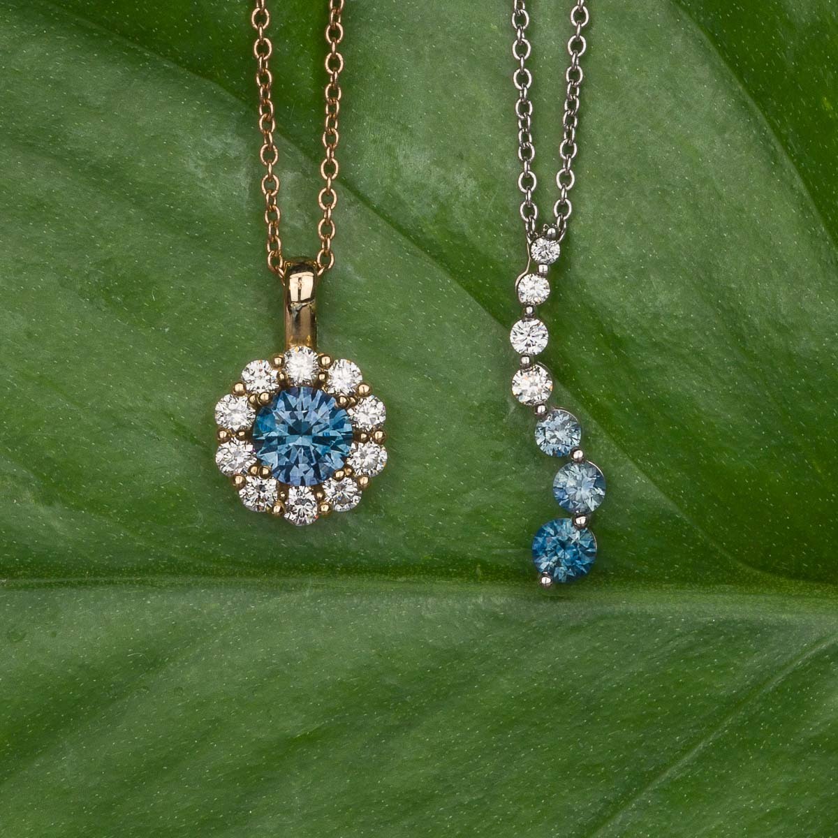 Two "Necklaces" with blue and white gemstones rest on a green leaf: one features a round halo pendant, while the other displays a vertical line of alternating gems.
