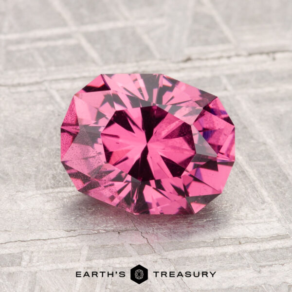 A 2.26-carat Mahenge Garnet, faceted in an oval shape, rests on a textured silver-gray surface with "EARTH'S TREASURY" displayed at the bottom.