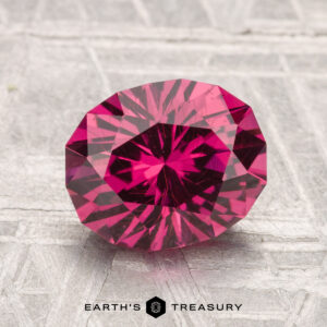 A 2.66-carat Mahenge Garnet with vivid pink-red hues is displayed on a textured gray surface with the Earth's Treasury logo below.