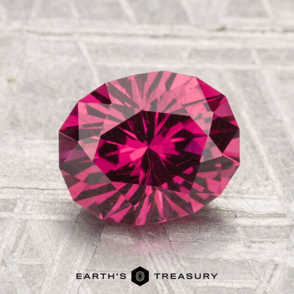 2.66-Carat Mahenge Garnet A 2.66-carat Mahenge Garnet with vivid pink-red hues is displayed on a textured gray surface with the Earth's Treasury logo below.