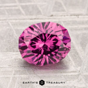 A faceted, oval-cut 2.22-carat Mahenge Garnet is displayed on a gray patterned background with the text "Earth's Treasury" at the bottom.