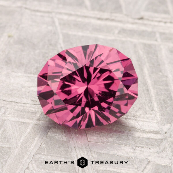 2.11-Carat Mahenge Garnet A 2.11-carat oval-cut Mahenge Garnet with intricate facets and a deep pink hue is displayed on a textured light gray surface, with "Earth's Treasury" shown below.
