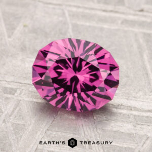 A 1.95-carat Mahenge Garnet, faceted in an oval cut, is displayed on a textured gray surface with the "EARTH'S TREASURY" text and logo at the bottom.