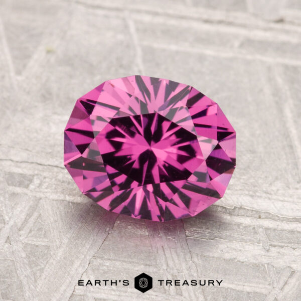 1.95-Carat Mahenge Garnet A 1.95-carat Mahenge Garnet, faceted in an oval cut, is displayed on a textured gray surface with the "EARTH'S TREASURY" text and logo at the bottom.