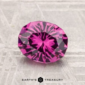 A vivid, faceted oval 1.90-carat Mahenge Garnet gemstone is showcased on a textured, light surface with "EARTH'S TREASURY" inscribed below.