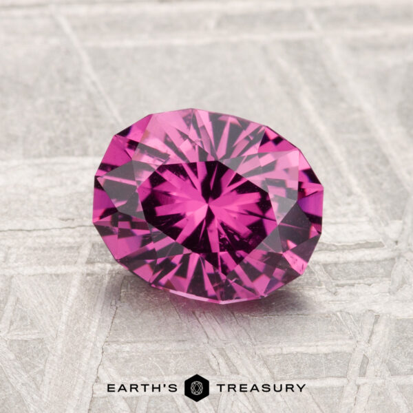 1.63-Carat Mahenge Garnet A 1.63-carat Mahenge Garnet, faceted in an oval cut, is displayed on a textured silver-gray surface with the text "EARTH'S TREASURY" below.