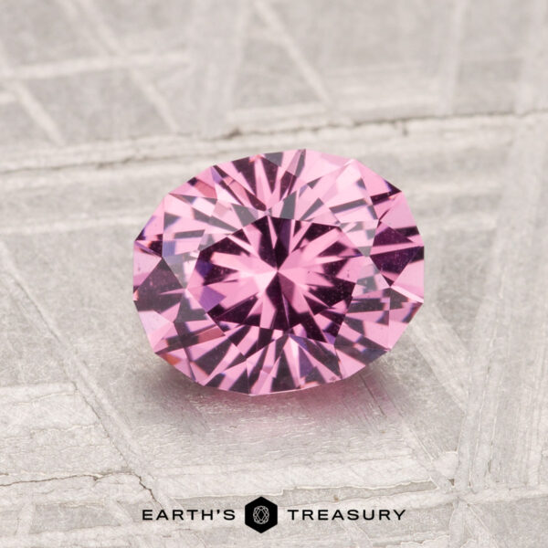 1.38-Carat Mahenge Garnet A 1.38-carat Mahenge Garnet, round brilliant-cut, is displayed on a textured light gray surface with "EARTH'S TREASURY" at the bottom.