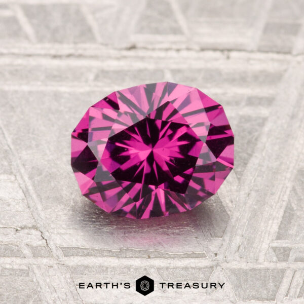 1.38-Carat Mahenge Garnet A 1.38-carat Mahenge Garnet, round and faceted, sits on a textured silver background with "EARTH'S TREASURY" displayed below.