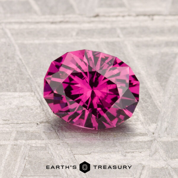 1.33-Carat Mahenge Garnet A 1.33-carat Mahenge Garnet, cut in a faceted oval shape, is showcased on a textured gray surface with the "Earth's Treasury" logo at the bottom.