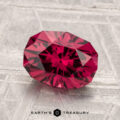 A faceted 2.37-carat Mahenge Garnet with a deep red hue rests on a textured silver-gray surface, with "Earth's Treasury" at the bottom.