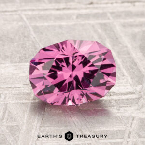 A faceted, oval-shaped 2.18-Carat Mahenge Garnet rests on a textured light gray surface, with the text "Earth's Treasury" below.