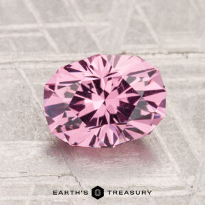 A 1.88-carat faceted oval Mahenge Garnet in light pink rests on a textured metallic surface, with "EARTH'S TREASURY" displayed at the bottom.