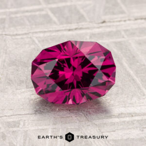 A faceted 1.87-carat Mahenge Garnet in deep pink is displayed on a light textured surface with "Earth's Treasury" at the bottom.