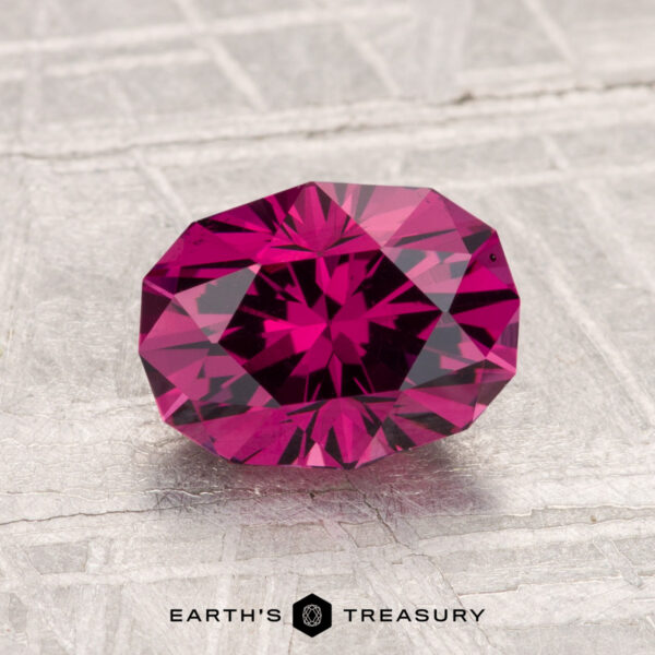1.87-Carat Mahenge Garnet A faceted 1.87-carat Mahenge Garnet in deep pink is displayed on a light textured surface with "Earth's Treasury" at the bottom.