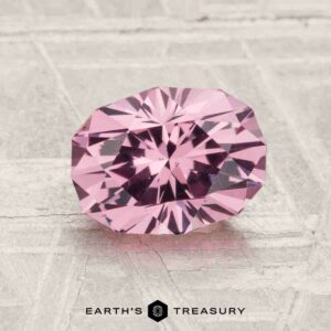 A 1.79-carat Mahenge Garnet with an oval cut and multiple facets is shown on a textured light gray surface, with the Earth's Treasury logo at the bottom.