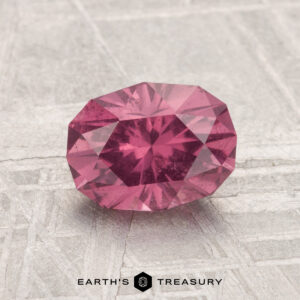 A 1.50-carat Mahenge Garnet, faceted in an oval cut, is displayed on a light textured surface with the text "EARTH'S TREASURY" at the bottom.