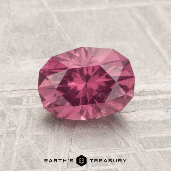 1.50-Carat Mahenge Garnet A 1.50-carat Mahenge Garnet, faceted in an oval cut, is displayed on a light textured surface with the text "EARTH'S TREASURY" at the bottom.