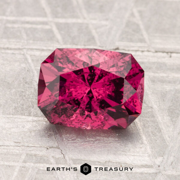 A 2.07-carat rectangular faceted Mahenge Garnet is shown on a textured gray surface with the "Earth's Treasury" logo and text beneath it.
