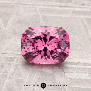 A 1.38-carat Mahenge Garnet with a rectangular radiant cut is displayed on a textured gray surface, with "Earth's Treasury" shown below.