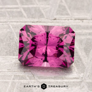 A 2.27-carat Mahenge Garnet with a radiant cut is shown on a textured light gray surface, with "EARTH'S TREASURY" displayed below.