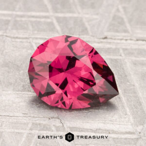 A 1.77-carat Mahenge Garnet, pear-shaped and faceted, is displayed on a textured gray surface with the "Earth's Treasury" logo at the bottom.
