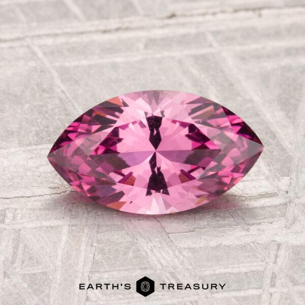 1.62-Carat Mahenge Garnet A 1.62-carat Mahenge garnet, marquise-cut and pink, rests on a textured light gray surface with “Earth’s Treasury” at the bottom.