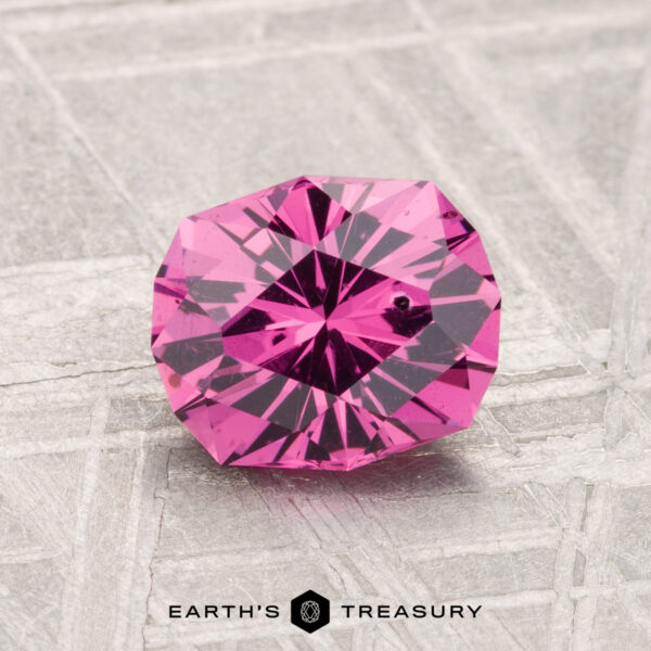 1.40-Carat Mahenge Garnet A 1.40-carat, round faceted Mahenge Garnet with a vivid pink hue is shown on a light-textured surface, featuring the "EARTH'S TREASURY" text at the bottom.