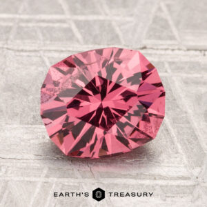 A 2.51-carat Mahenge Garnet with a pink hue rests on a textured silver surface, featuring the "Earth's Treasury" logo at the bottom.