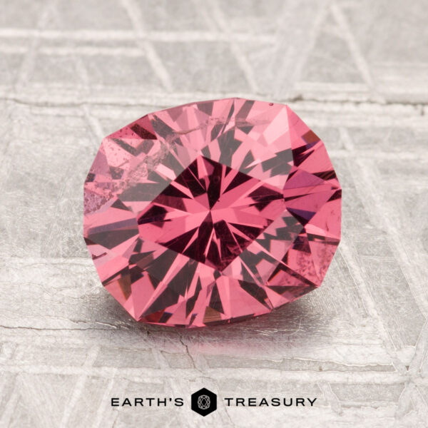 2.51-Carat Mahenge Garnet A 2.51-carat Mahenge Garnet with a pink hue rests on a textured silver surface, featuring the "Earth's Treasury" logo at the bottom.